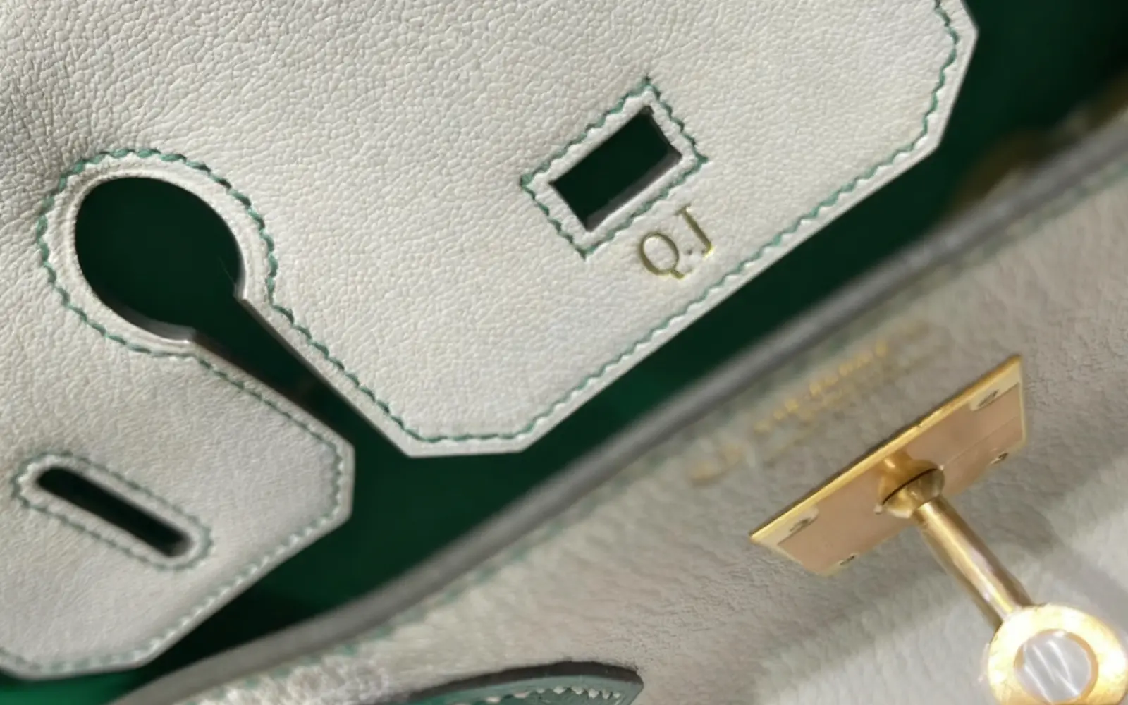 Gold initials applied to pale leather beside hand-finished stitching and hardware